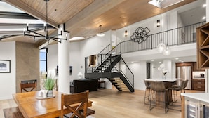 A spacious kitchen with a central island, a dining area with a wooden table and chairs, and a staircase leading to an upper level.