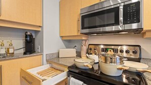 Uma cozinha moderna com micro-ondas de aço inoxidável, máquina de café, torradeira e fogão com panelas e frigideiras.