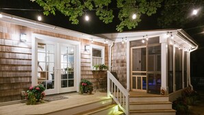 Een houten huis met een overdekte veranda, witte deuren en lichtjes.