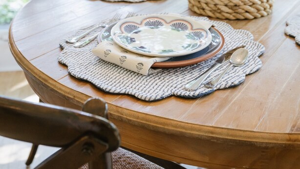 Een eettafel gedekt met borden, bestek en een kaars in een kamer met grote ramen en uitzicht op bomen.