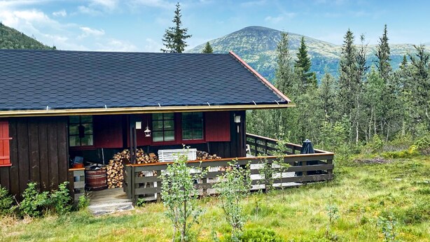 A rustic cabin with a dark roof, wooden exterior, and a porch with a railing. - 3 bedroom beautiful home in Tynset (Tynset)