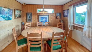 Ein Esszimmer aus Holz mit einem runden Tisch und sechs Stühlen, gerahmten Bildern an den Wänden und einem Fenster mit Vorhängen.