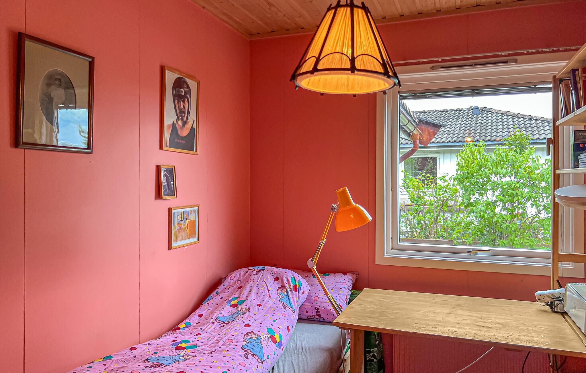 Une pièce avec un lit, un bureau et une fenêtre. Des tableaux encadrés ornent le mur.