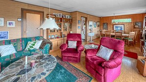 Ein gemütliches Wohnzimmer mit einem grünen Sofa, zwei roten Sesseln, einem Marmor-Couchtisch und einem Essbereich mit Holzmöbeln.