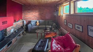 Ein gemütliches Zimmer mit Backsteinwand, Ledersofa, rotem Sessel, kleinem Tisch und Fenster mit Blick auf Grünfläche.