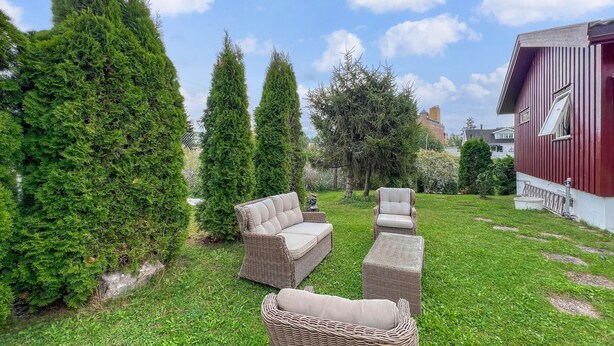 Ein Garten mit Sitzgelegenheit, hohen Bäumen und einem roten Gebäude.