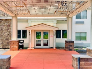 A building entrance with a covered walkway, double doors, and a stone wall on one side.