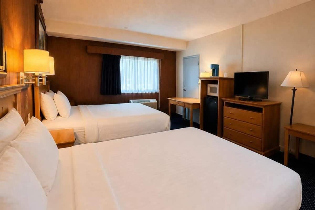 A hotel room with two beds, a desk with a television, a microwave, and a lamp.