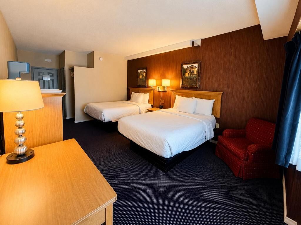 Ein Hotelzimmer mit zwei Betten, einem Schreibtisch, einem Stuhl und einer Lampe.