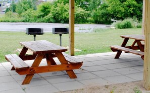 A picnic table with a wooden bench, a metal pole, and a trash bin. - Travel Inn (Watertown)
