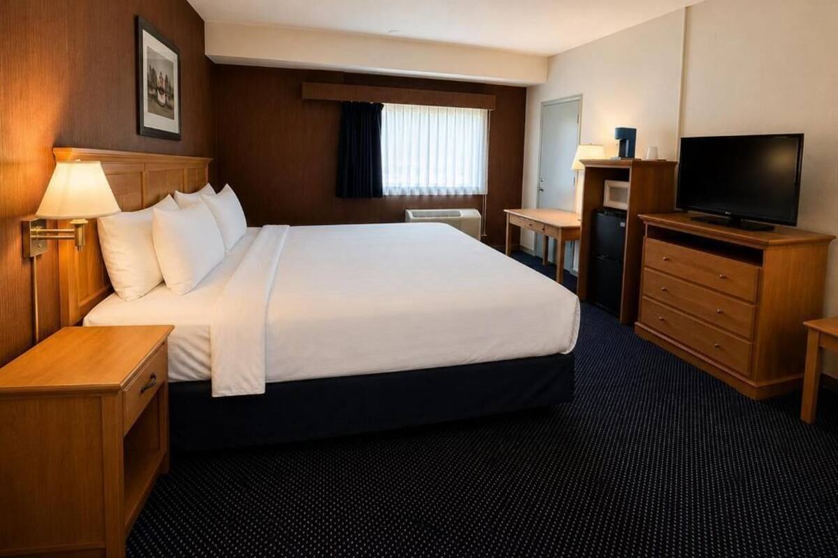 A hotel room with a bed, bedside tables, a desk with a chair, a television, and a window with curtains.