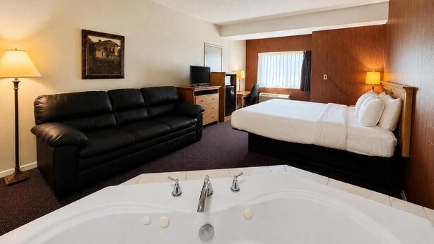 Habitación de hotel con una bañera grande, un sofá de cuero negro, una cama, un escritorio con ordenador y televisión.