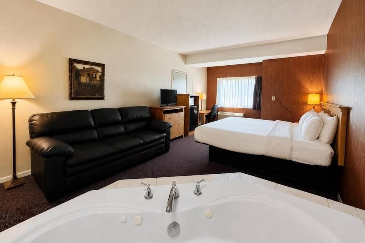 A hotel room with a large bathtub, a black leather sofa, a bed, a desk with a computer, and a television.