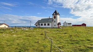 A white church with a red tower and a smaller building in a grassy field.