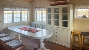 A dining area with a white table, cushioned chairs, a cabinet with glass doors, and a view of the water outside.