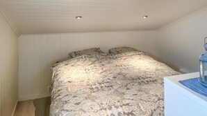 A bedroom with a bed, two ceiling lights, and a nightstand with a lamp.