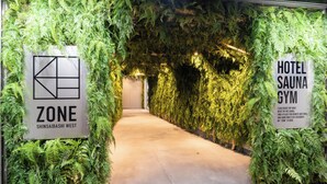 A hallway with a green wall covered in ferns leading to a door labeled "HOTEL SAUNA GYM". - ZONE SHINSAIBASHI WEST (Osaka)