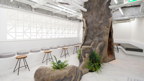 A modern interior with a large tree trunk centerpiece, seating areas, and a geometric window design. - ZONE SHINSAIBASHI WEST (Osaka)