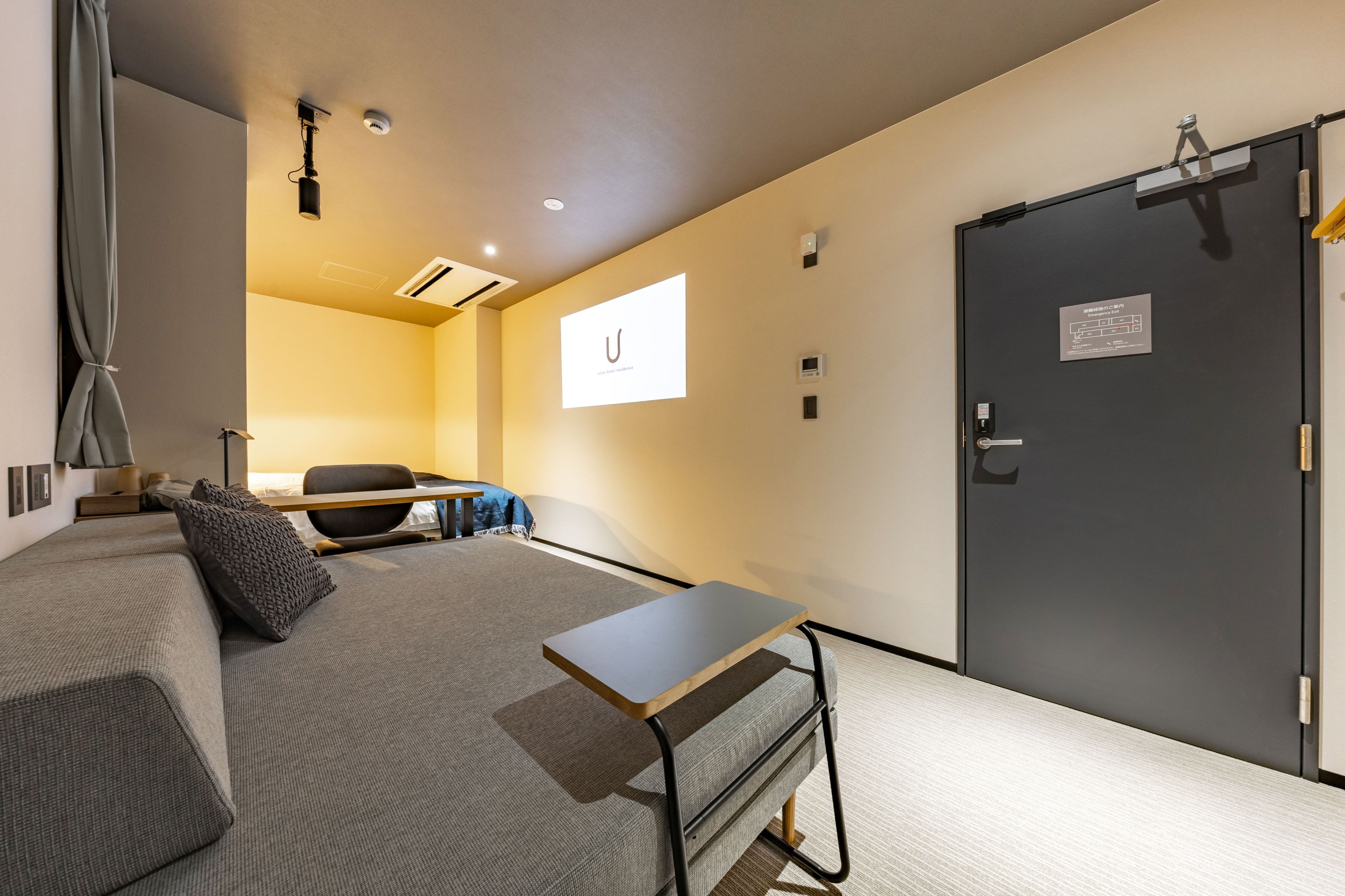 Une chambre d’hôtel comprenant un lit, un bureau, une chaise, une armoire et une porte avec un panneau indiquant la sortie de secours.
