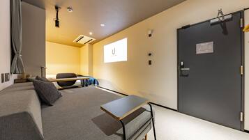 A hotel room with a bed, a desk, a chair, a wardrobe, and a door with an emergency exit sign.