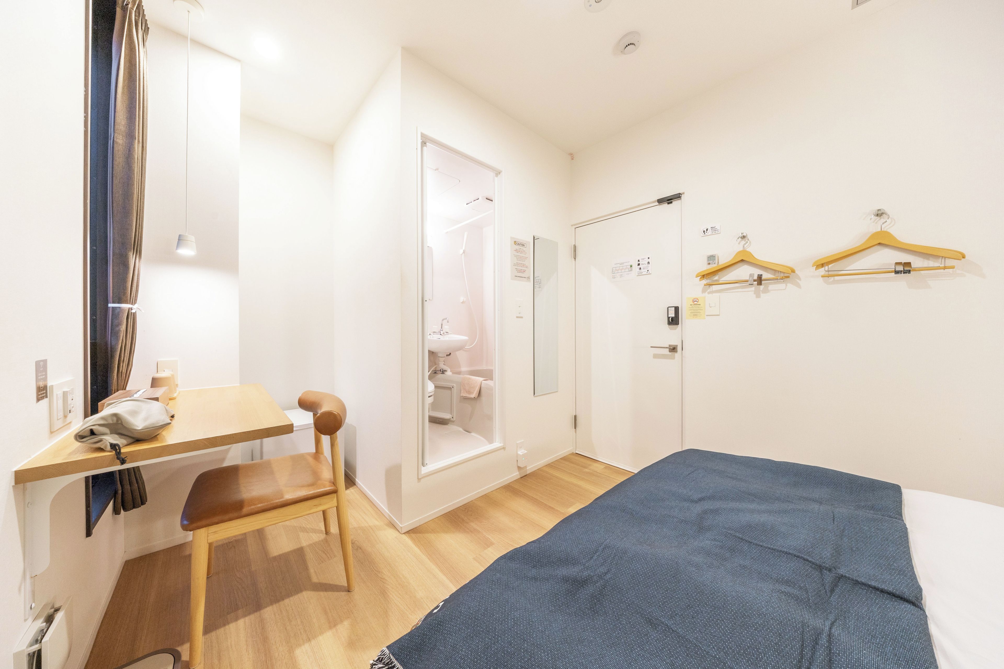 A hotel room with a bed, a desk with a chair, a shower area, and a wardrobe.