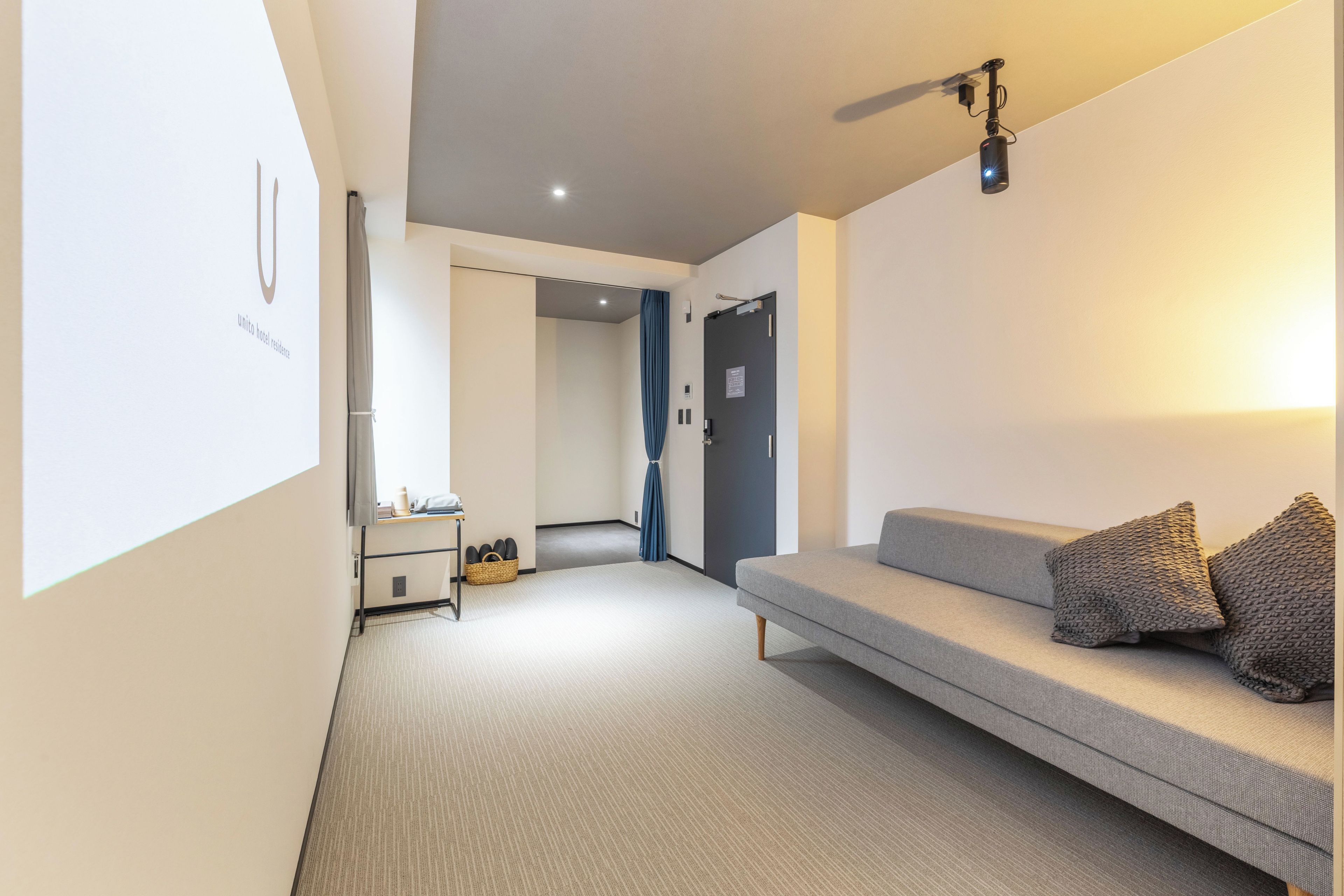A hotel room with a sofa, a small table, a basket, and a ceiling-mounted projector.
