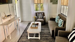 A living room with a wooden coffee table, a sofa, a chair, a TV mounted on the wall, and a window with curtains.