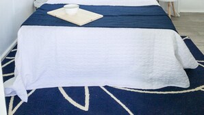 A neatly made bed with a blue and white bedspread, a white pillow, and a tray with a cup and bowl.