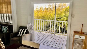 A cozy living room with a sliding glass door leading to a wooden deck, a fan, and a small table with a decorative item.