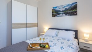 Une chambre à coucher comprenant un lit, une table de chevet, une commode, une armoire et un tableau représentant un paysage de montagne.