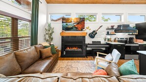 A cozy living room with a fireplace, a piano, and a guitar on the wall.
