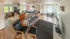 A spacious living area with a gray sofa, black leather chairs, a dining table with blue chairs, and a fireplace. - Cozy home in åhus with sauna (Åhus)
