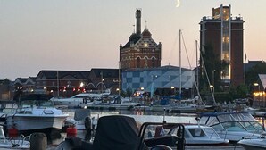 A marina with boats docked, a prominent building with a clock tower, and a crescent moon in the sky. - Cozy home in åhus with sauna (Åhus)