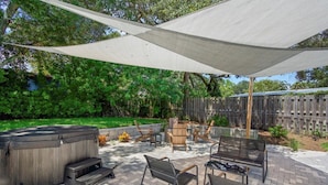 An outdoor patio with a hot tub, seating area, and a large canopy providing shade.
