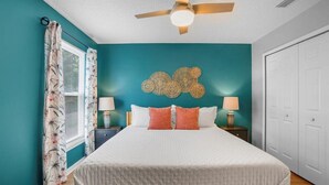 A bedroom with teal walls, a white bedspread, two bedside lamps, and a ceiling fan.