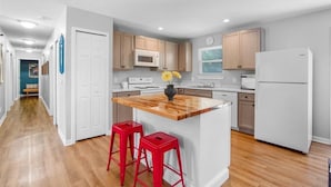 A modern kitchen with wooden countertops, white cabinets, and a central island with red stools.
