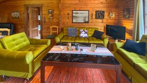 L’intérieur d’un chalet confortable, avec des murs en bois, un canapé vert, une table basse et un téléviseur.