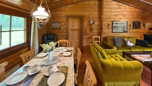 L’intérieur d’un chalet en bois comprend une table à manger dressée pour quatre personnes, un canapé vert et un plafond en bois.