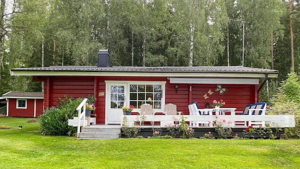 Une cabane en bois rouge avec un porche, des meubles d’extérieur blancs et un jardin.