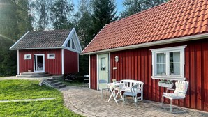 Une maison en bois rouge avec un toit en tuiles, une véranda à l’avant avec des chaises blanches et une petite table.