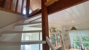 Un escalier en bois mène à une pièce comprenant un coin cuisine, une fenêtre donnant sur un espace verdoyant et un ventilateur de plafond.