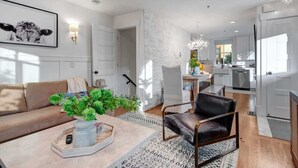 A modern living room with a sofa, a chair, a coffee table with a vase, and a kitchen in the background.