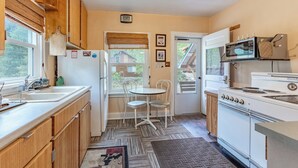 A compact kitchen with wooden cabinets, a white refrigerator, a microwave, a stove, and a dining area with a small table and chairs. - Papa's Cottage- Dog Friendly- Close to Monarch (Salida)