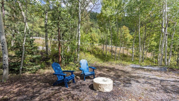 An outdoor seating area with two blue Adirondack chairs and a round table, surrounded by trees and a dirt path. - Papa's Cottage- Dog Friendly- Close to Monarch (Salida)