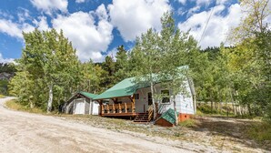 A rustic cabin with a green roof, wooden deck, and a garage. - Papa's Cottage- Dog Friendly- Close to Monarch (Salida)