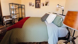 A bedroom with a bed, a bench, a lamp, and a wall with framed pictures.