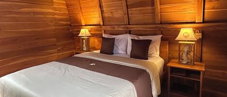 Un dormitorio de cabaña de madera con una cama, dos mesitas de noche y dos lámparas.