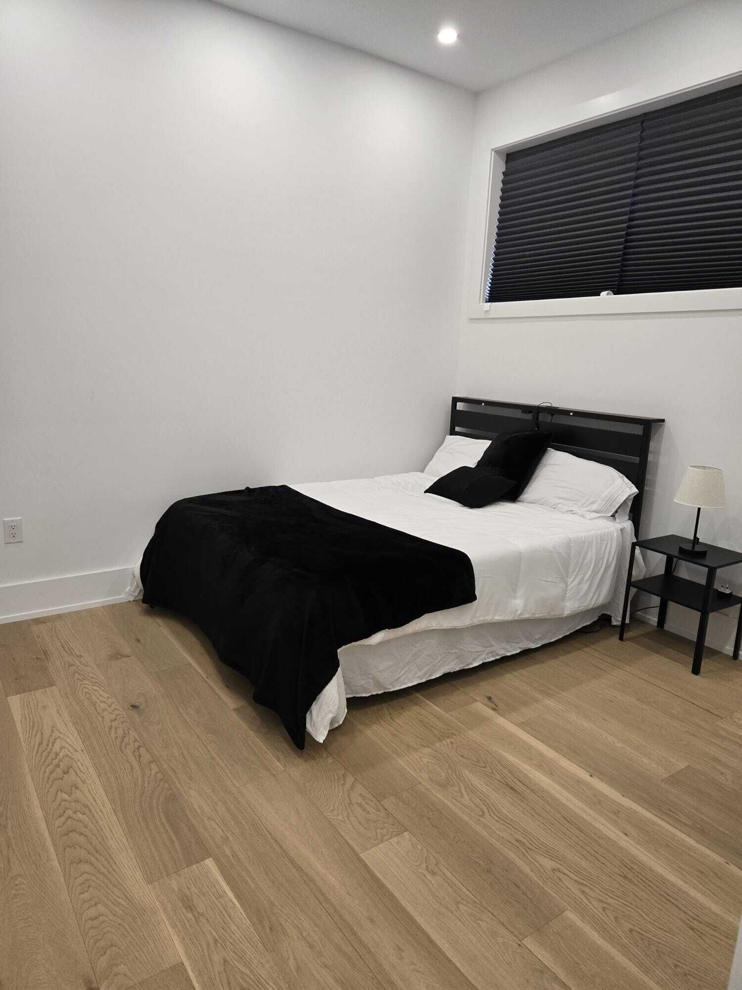 A bedroom with a bed, a nightstand, a lamp, and a window with blinds.