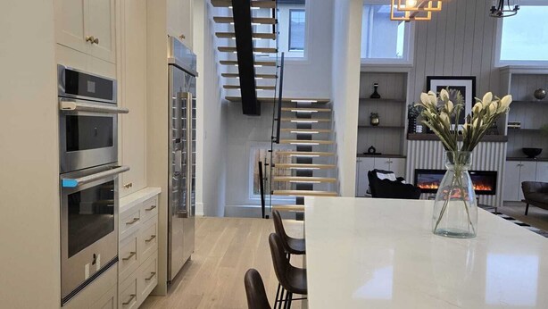 A modern kitchen with built-in appliances, a central island with bar stools, and a staircase leading to an upper level. - Luxury 5 BR, Gym, Sauna, Thtr, OD FP & Ktcn, Lake (Burlington)