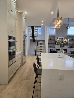 A modern kitchen with built-in appliances, a central island with bar stools, and a staircase leading to an upper level. - Luxury 5 BR, Gym, Sauna, Thtr, OD FP & Ktcn, Lake (Burlington)